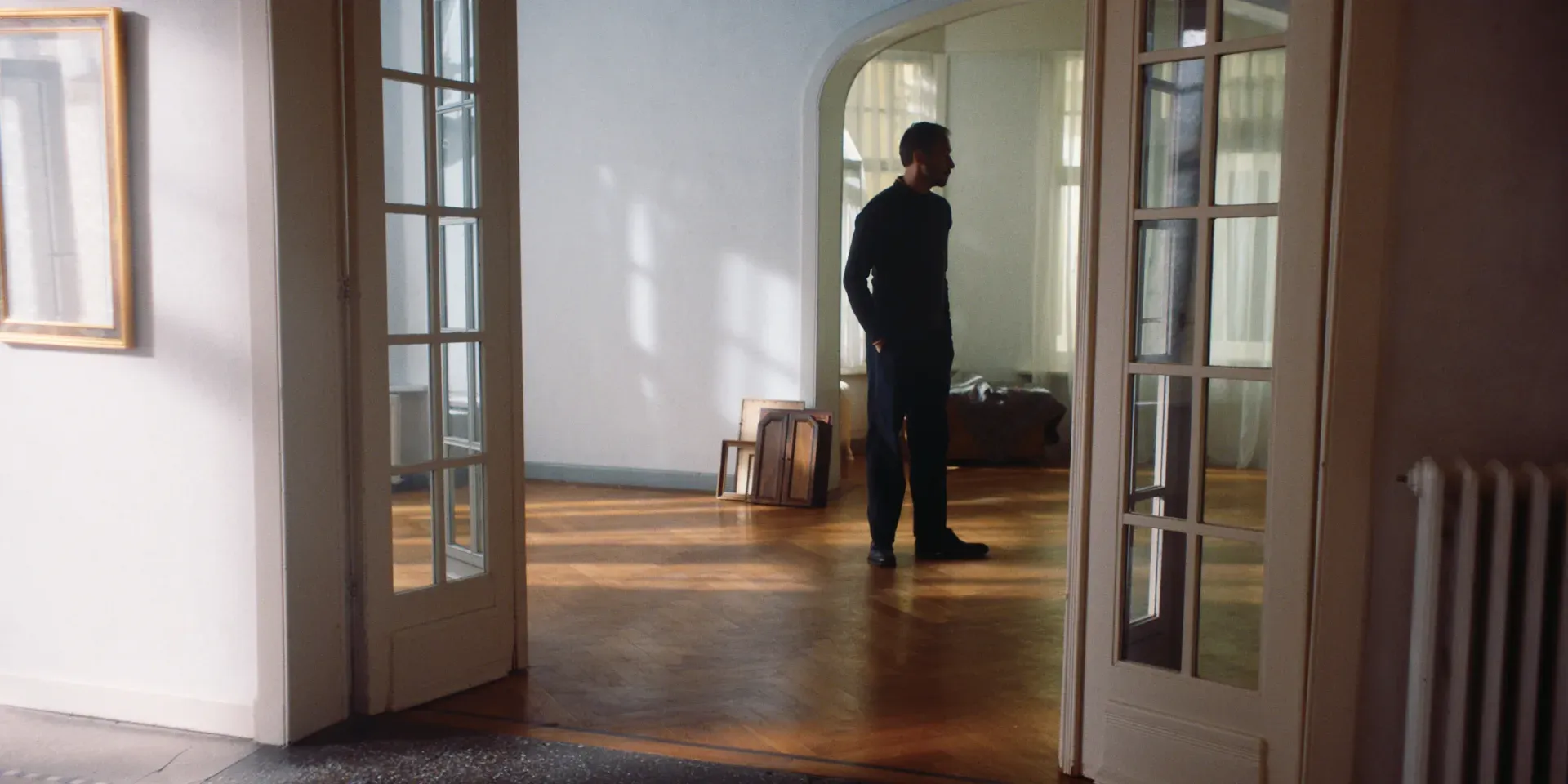 Ana's husband standing alone in a sparsely furnished room in The Tears of Things