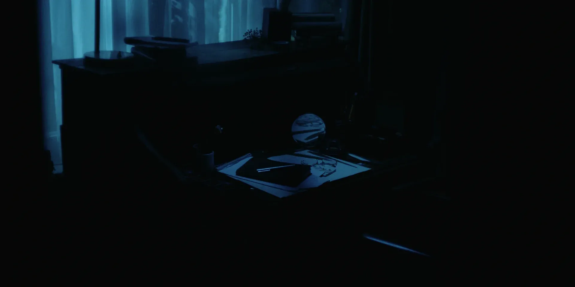 A writing desk with papers, glasses, and a round mirror in The Tears of Things