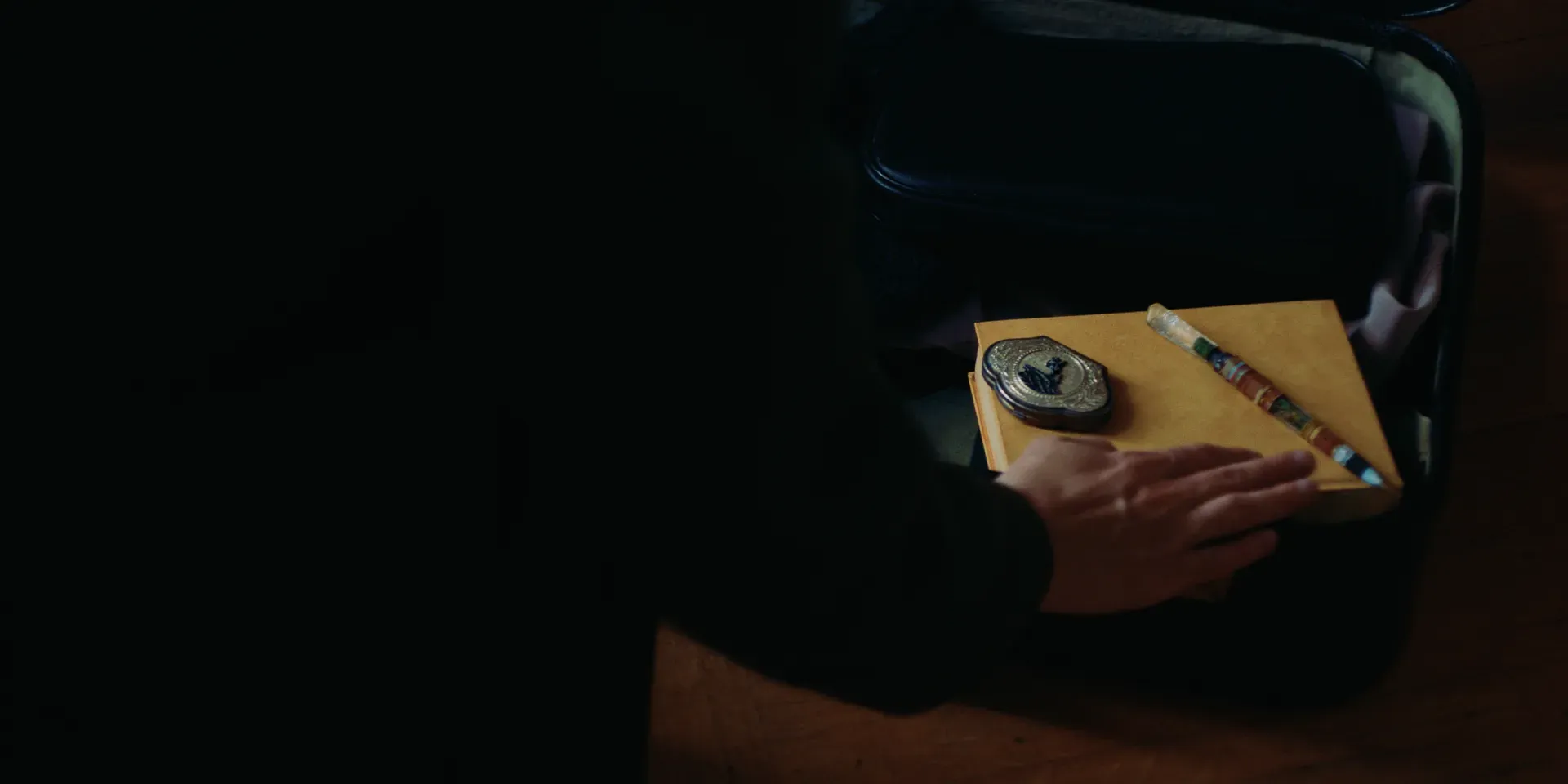 A hand resting on a yellow diary beside a pen and locket in The Tears of Things
