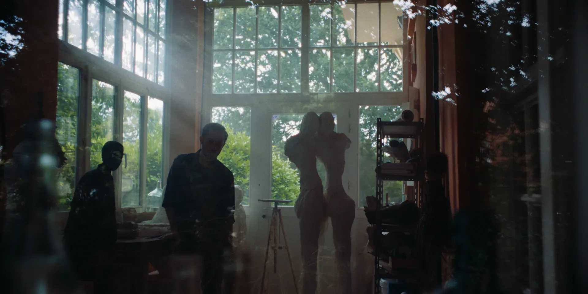 Two figures reflected in the window of a sculpture studio in The Tears of Things
