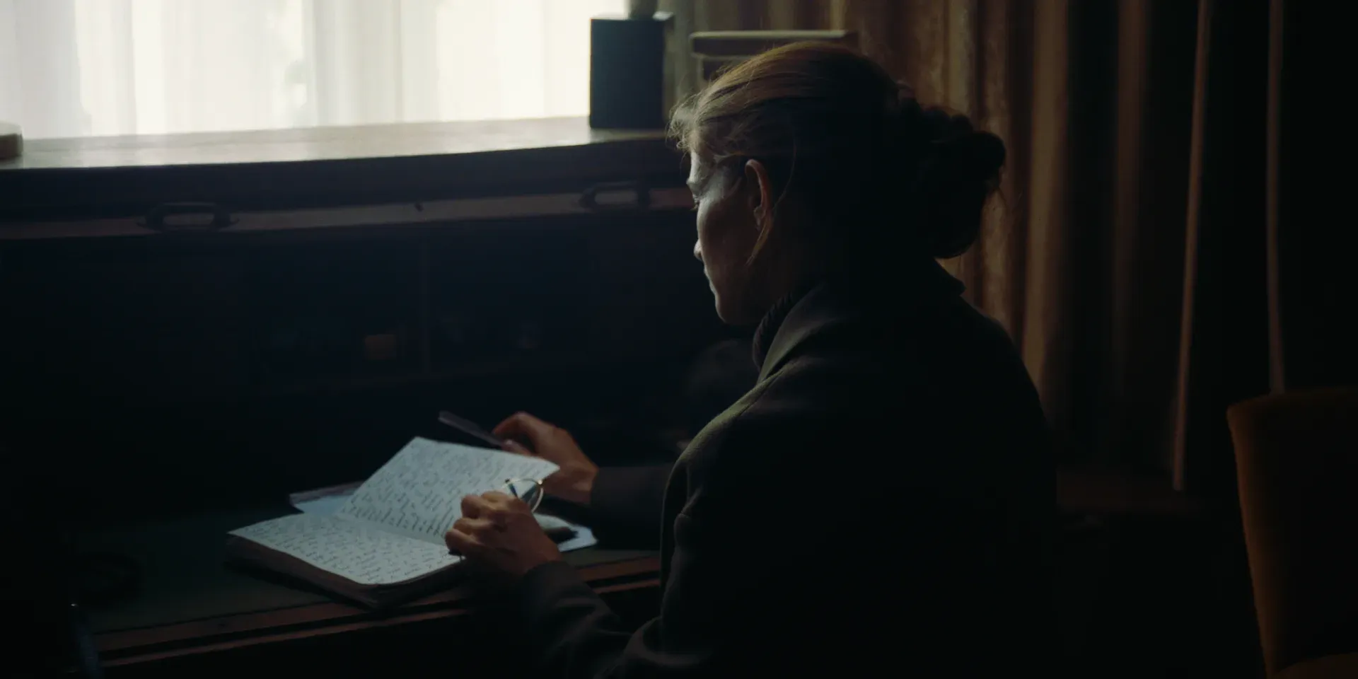 Ana seated at a desk writing beside a window in The Tears of Things